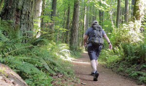 A man wearing a weighted backpack walks on a hiking trail.