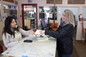 A women is handed her recently purchases fishing license across the counter of a license dealer.